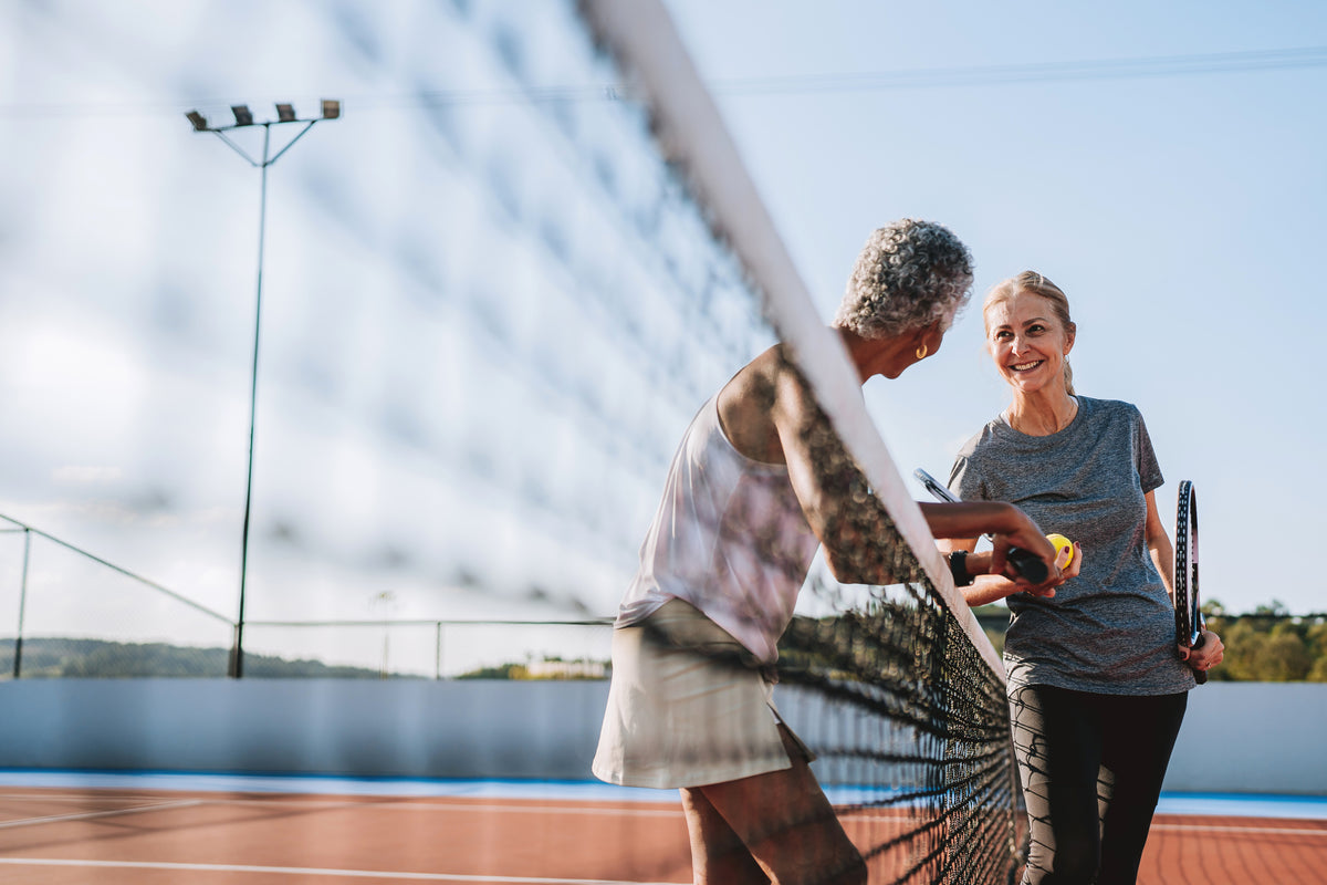 Two women smiling at each other across a tennis net